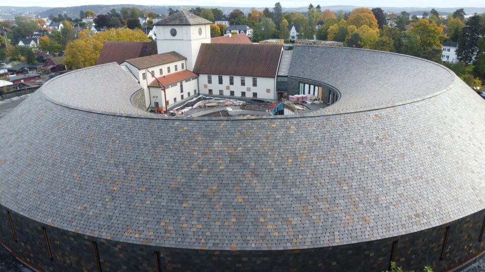 Den nye delen av Vikingtidsmuseet reiser seg på Bygdøy, med et tak som kombinerer tradisjonelt håndverk og moderne presisjon. Den gamle delen av museet skimtes i bakgrunnen. Foto: Marius Lysø