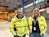 To personer i gule Moelven-jakker står i en stor produksjonshall innendørs.
