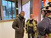 Tre menn snakker sammen inne i et moderne bygg med store vinduer og byggeklær.