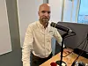 Mann ved podcastmikrofon i studio, stående ved skrivebord.