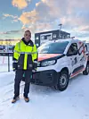Person i refleksjakke står foran firmabil på snødekt område ved næringsbygg.