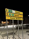 Veiskilt som viser retning mot Kirkenes og Grense Jakobselv en mørk vinterkveld.