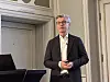 Mann i dress holder presentasjon foran talerstol i konferanserom. hent