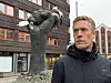 Mann i mørk jakke står foran stor knyttneve-skulptur på et bytorv.