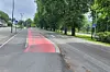 Rødmerket sykkelfelt langs en bred vei med trær og gangfelt i grønt bymiljø.