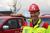 Person i Risa-hjelm og gul anleggsjakke står foran røde servicebiler utendørs.