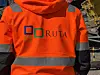 Rygg til person i oransje RUTA-refleksjakke på bygge- eller anleggsplass.