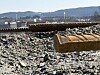 Rustent armeringsjern ligger i grus med industriområde og åser i bakgrunnen