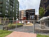 Inngjerdet byggeplass med gravemaskin og skilt mellom høye boligblokker.