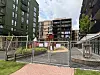 Inngjerdet byggeplass med gravemaskin og skilt mellom høye boligblokker.