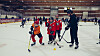 Unge ishockeyspillere og en trener står på en isflate i en innendørshall.