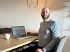 En mann sitter ved et bord med en åpen bærbar PC og en kopp på et hjemmekontor.