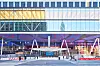 Moderne fasade med glass og metall foran en stasjon, med stillaser, sperringer og noen personer på plassen.