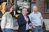 Tre personer står foran en byggeplass med anleggsmaskiner og murbygninger i bakgrunnen.