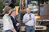 Tre personer står foran en gravemaskin på en anleggsplass utendørs.