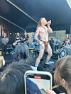 En bar overkropp kledd mann med langt hår står på en scene og opptrer foran et publikum.
