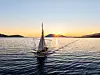 En liten seilbåt på stille sjø med solen lavt over horisonten.