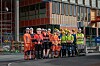 En gruppe personer i verneklær og hjelmer står foran et stort bygg under oppføring.
