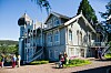 Blå og hvit historisk villa med tårn, trapper og folk samlet utenfor i solskinn.