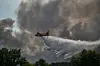Et vannbombefly slipper vann over en skogbrann med store røykskyer over trærne.