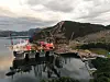 Stort offshoreanlegg ved kai med kraner, røde fartøy og fjell i bakgrunnen.