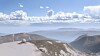 En hvit radom på en fjelltopp med fjell og skyer i bakgrunnen.