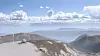 En hvit radom på en fjelltopp med fjell og skyer i bakgrunnen.