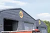En stor grå hall med B&G Tunnel-logo på veggen og utstyr stablet foran bygget.