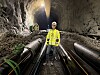 Person i verneutstyr står mellom store rør inne i en fjellhall med gruslagt gulv og belysning i taket.