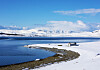 Snødekt kystlinje ved en delvis islagt fjord med en liten bygning og fjell i bakgrunnen.