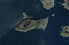 Luftfoto av en øy omgitt av mørkt vann, med kystlinje, veier og spredt bebyggelse.