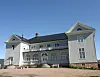 Stor, hvit historisk bygning med flere vinduer og takkonstruksjoner under blå himmel.