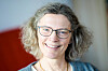 Smilende kvinne med briller foran en lys bakgrunn.