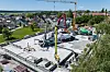Byggeplass med betongdekke, kraner og maskiner som arbeider ved et halvferdig bygg.