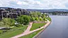 Utsikt over en park med gangveier og trær langs en elv, med bygninger i bakgrunnen.