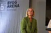 En kvinne i grønn dress står foran en scene med Bygg Arena Arendal-banner i bakgrunnen.