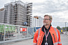 En mann i oransje vernejakke står foran en innhegnet byggeplass med stillas på en bygning.