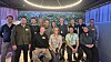 En gruppe mennesker poserer sammen i et mørkt lokale med dekorativ belysning.
