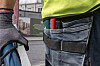 Nærbilde av en person i arbeidsklær med hanske, verktøybelte og håndverktøy utendørs.