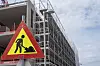 Gult trekantet varselskilt foran et stort bygg under oppføring med stillas.