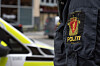 Nærbilde av en uniformert politibetjent foran en hvit patruljebil med gule og svarte detaljer.