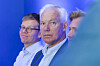 Tre menn står foran en blå bakgrunn, med en hvithåret mann i skjorte og jakke i forgrunnen.
