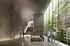 Arkitektillustrasjon av en underjordisk utstillingshall med besøkende, trapp og glassvegg mot grønne omgivelser.