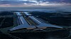 Oversiktsillustrasjon av et enormt, opplyst industribygg i et mørkt og flatt landskap.