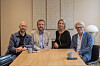 Fire personer sitter samlet rundt et bord i et lyst møterom.