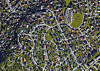 Flyfoto av et tett boligområde med hus, veier, hager og grønne arealer.