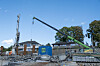 Anleggsområde med kraner, byggegrop, gjerder og bygninger under en blå himmel.