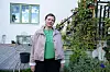 Kvinne står på en terrasse foran et hus, omgitt av planter og hagemøbler.