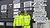 To personer i gule synlighetsklær står foran et skilt med stedsnavn på Svalbard.