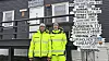 To personer i gule synlighetsklær står foran et skilt med stedsnavn på Svalbard.